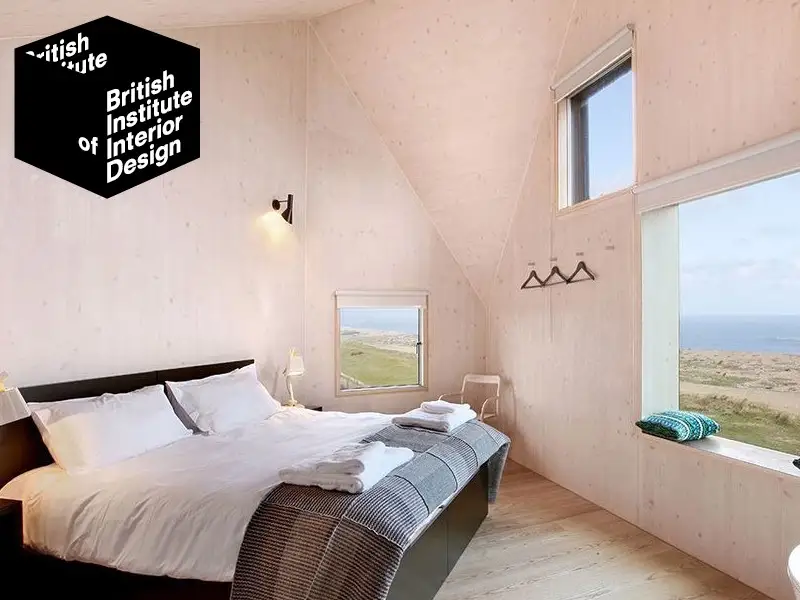 wooden lined bedroom with a high vaulted style ceiling in a minimalist design overlaid with the BIID British Institute or Interior Design logo