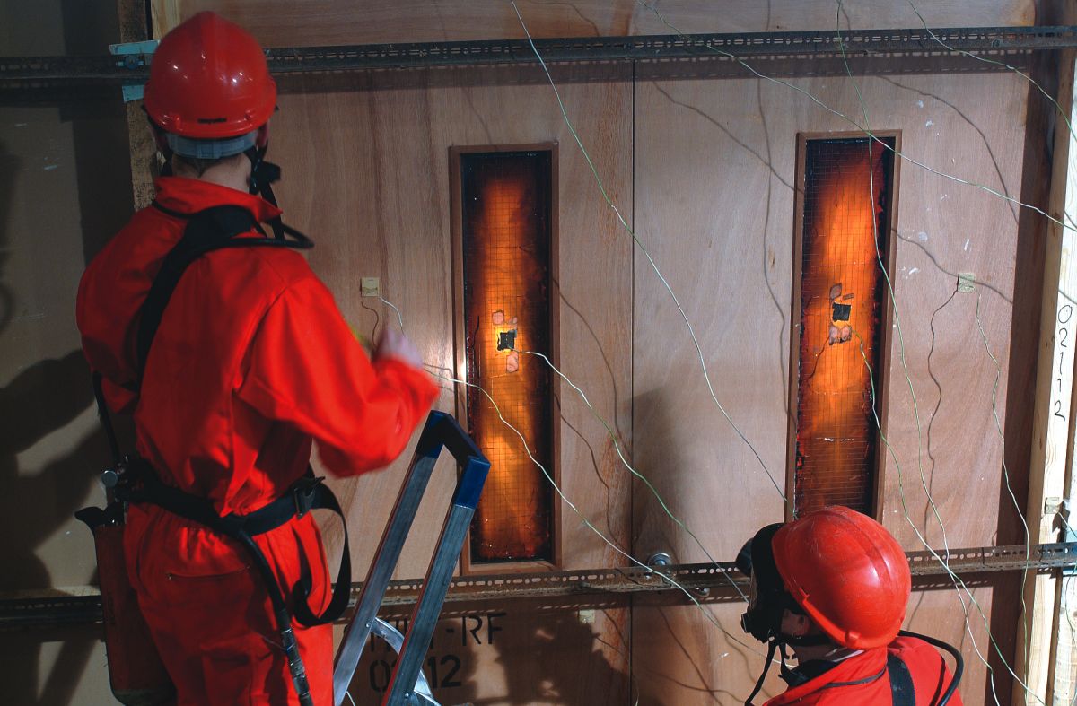 two operatives working in protective clothing during fire resistance testing on fire doors 
